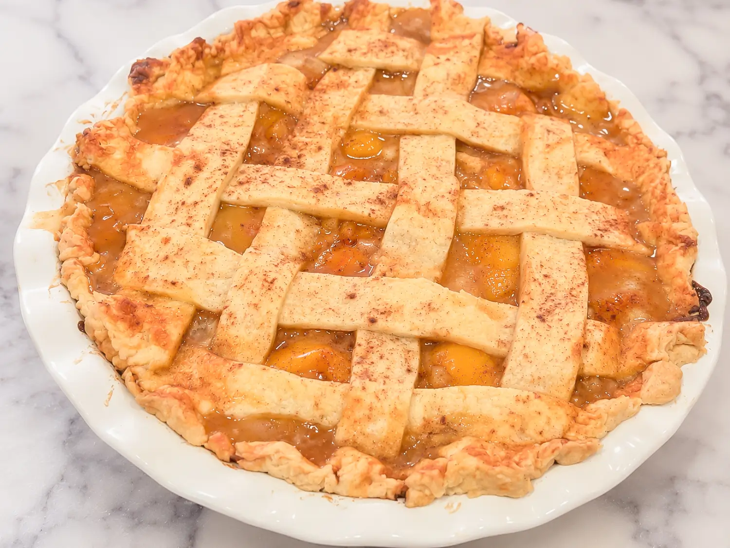 HERO homemade peach pie recipe in a white baking dish on a marble surface