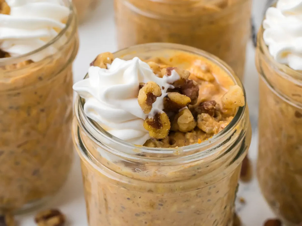 close up photo of walnuts and cream on top of a mason jar filled with pumpkin overnight oats