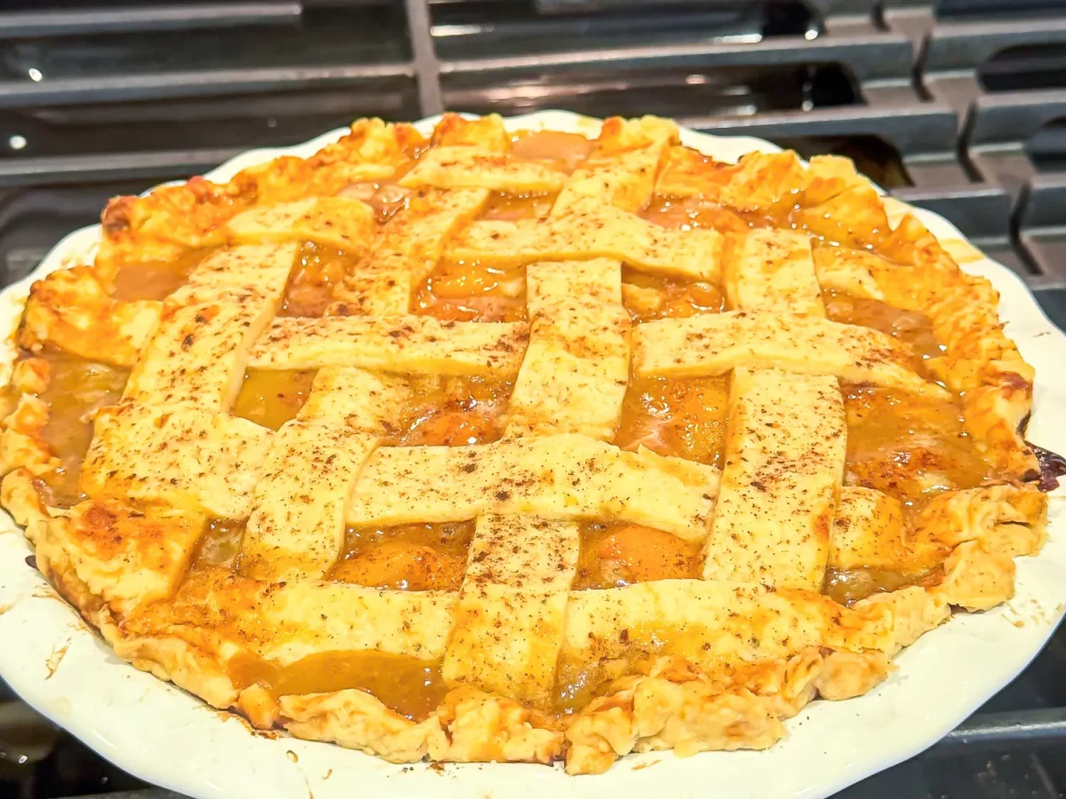 close up photo showing a peach pie resting on a stove top out of the oven