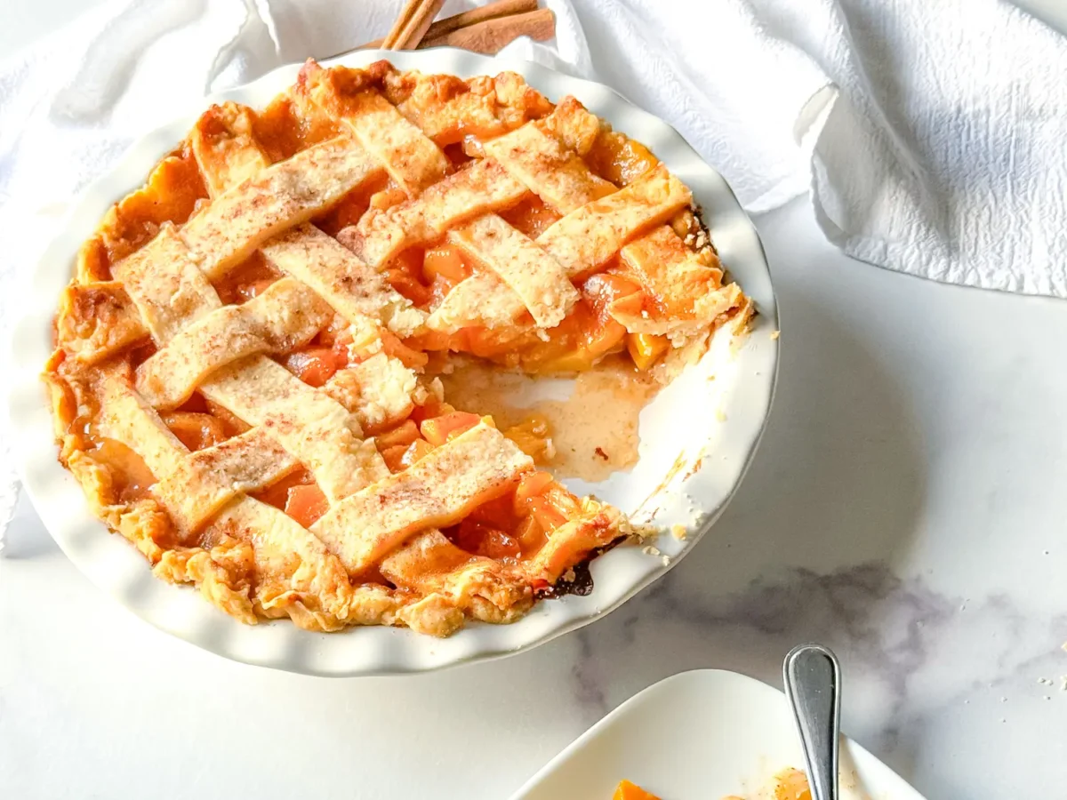 close up photo showing a peach pie with a slice of pie missing