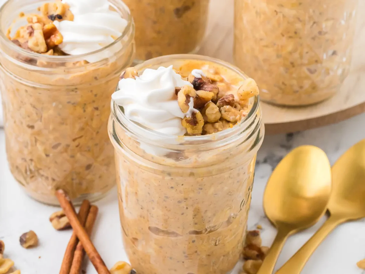 photo of pumpkin overnight oats in a mason jar next to gold spoons and cinnamon sticks