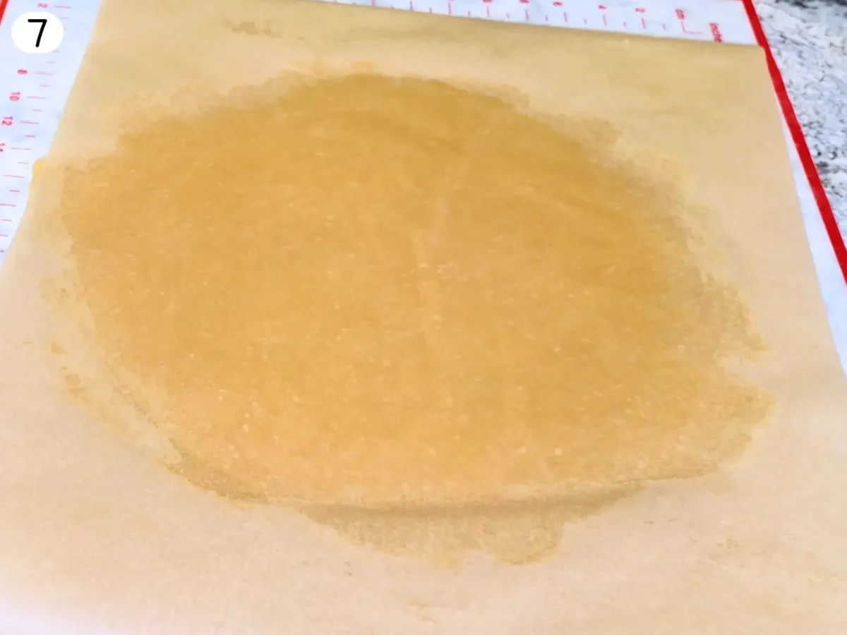 step 7 photo showing pie dough rolled out in between two sheets of parchment paper